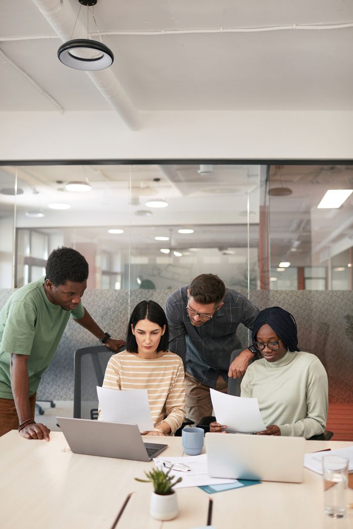 A group of diverse professionals collaborating in a modern office setting, focusing on documents and laptops.